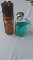 Photo showing two fragrance bottles: brown Cuba Paris after shave spray and clear triangular Nautica cologne.