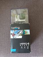 Front view of GoPro HERO4 Black camera in waterproof housing inside original box showing branding and waterproof depth rating.