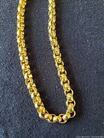 Close-up image showing the interlocking links of the gold tone belt chain on a dark fabric background.