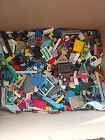 Top-down view of box filled with assorted LEGO pieces of various colors and shapes showing classic bricks, plates, and window frames.