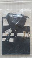 Photo of one men's designer black and white shirt folded in plastic packaging showing tags and 'Saint-Tropez France' embroidery.