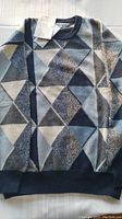 Blue, grey, and white geometric triangle pattern men's sweater laid out flat on white surface.