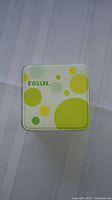 Closed Fossil branded tin box with green and yellow circular design on top.