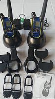 Photo showing two Motorola walkie-talkie radios in black charging docks accompanied by belt clips and multiple interchangeable faceplates, plus an instruction manual.