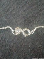 Close-up image showing the spring ring clasp and chain links of a silver curb chain necklace.