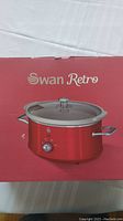 Photo of the front of the product box showing the Swan Retro slow cooker in red with stainless steel handles and dial knob.