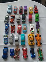 Top view of a diverse collection of 25 toy cars including Hot Wheels and other brands in a variety of colors and models on white surface.