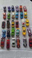 Top-down view of 31 Hot Wheels toy cars arranged in rows on a white surface, showing a variety of colors and designs.