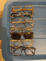 Seven pairs of prescription glasses arranged in a row on a blue surface, showing different styles and colors.