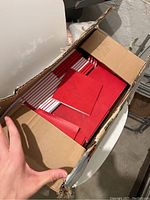 Open box showing numerous red square notebooks inside, stacked neatly.