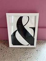 Front view of the framed ampersand art print against a pink wall and speckled surface.