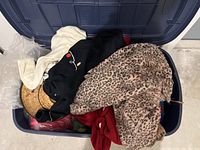 Large bin filled with various costume items including pink leopard faux fur coat, black knit sweater, and other assorted clothing items.