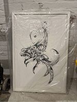 Front view of framed black and white abstract art print wrapped in plastic against a brick wall background