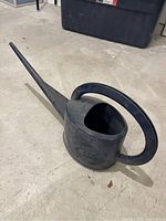 Large dark blue plastic watering can placed on concrete floor showing full length and shape