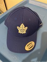 Front view of navy blue hat showing white Toronto Maple Leafs embroidered logo and snapback sticker on brim.