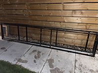 Wide view of two black rectangular metal frames laid on ground in front of wooden fence.