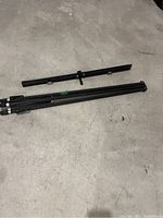 Photo showing folded black metal tripod stand and separate horizontal crossbar.