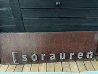Front view of large rectangular weathered metal sign with silver raised letters spelling 'sorauren'.