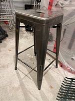 Front left angled view of gunmetal metal counter height stool showing square seat with handle cut-out and leg structure