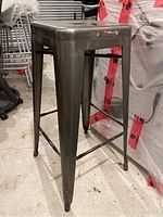 Side angle photo of gunmetal metal bar stool showing sturdy tapered legs and square seat.