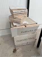 Stacked boxes labeled 'nanda tiles' with some white square tiles stacked on top