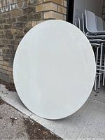 White round tabletop leaning vertically against a brick wall, showing the top surface with scratches visible.
