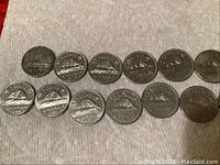 Photo of 15 circulated Canadian 5-cent coins arranged in two rows on a light-colored fabric surface, clear details of the beaver design and dates on the reverse side visible.