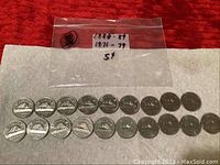 19 Canadian nickels arranged on fabric, some in clear plastic bag labeled with years 1980-89 and 1971-79.