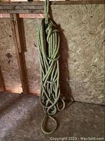 Coiled natural fiber rope hanging against a wooden wall, showing thickness and condition.