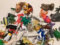 Photo showing a collection of mostly loose marine animal plastic toys in various colors and species such as sharks, fish, penguins, seals, and turtles, arranged on a white surface.