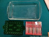 Set of three items including clear glass casserole dish, green glass server, and boxed set of 12 serving forks on green surface.