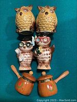 Three sets of salt and pepper shakers including owl designs and small pots, arranged on turquoise fabric background