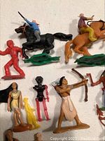 Top view of various plastic toy figures showing Native American and cowboy characters, mounted and on foot, along with toy weapon accessories.