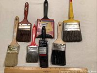 Photo showing top view of 7 paint brushes of different sizes and handle colors