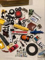 Wide view of assorted toy car and vehicle parts scattered on a white surface, showing variety and condition of items
