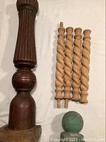 Large dark-stained carved wooden piece with base, four lighter spiral turned wooden pieces, and small green decorative spherical topper on a white surface