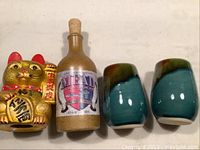 Image of golden cat bank, ceramic Mead bottle, and two ceramic tumblers