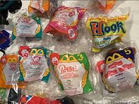 Close-up of multiple unopened McDonald's Happy Meal toys in original plastic packaging showing Babe, VR Troopers, Hook, and others.
