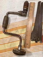 Photo showing vintage hand drill alongside a ruler and several metal shelf supports in orange and black.