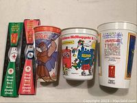 Two McDonald's Official Olympic watches in original packaging alongside three vintage McDonald's collectible cups including a Hercules Disney-themed cup, Chicken McNuggets & Coke cup, and an Olympic Centennial Games cup.