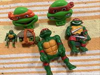Photo showing several Teenage Mutant Ninja Turtles figures including one small figurine with backpack, three larger figures, and two plastic turtle head moulds in green and orange/red.