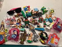 Overview of various small collectible toys including Disney and Looney Tunes characters and loose items scattered on a white surface