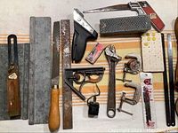 Photo showing assorted tools including hand saw, files, clamps, adjustable wrench, and miscellaneous hardware parts on a striped cloth