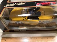 Side view of yellow Mustang Mach III die-cast model car inside its original unopened plastic display case showing detail and scale with ruler below.
