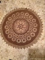 Top-down image of circular mat laid on tiled floor showing scalloped edges and crocheted flower patterns.