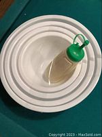 Photo showing nested white vinyl bowls alongside beige and green sauce dispenser.