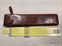 Brown leather case with marks, positioned above the yellow Pickett 500 slide rule showing overall length and condition.