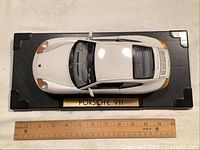 Top view of the white Porsche 911 model car on black display stand with ruler for size reference