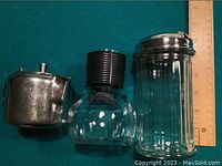 Side view of the three vintage containers showing metal cream pitcher, glass water bottle, and ribbed sugar dispenser next to a ruler for size reference.