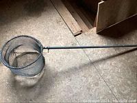 Full view of vintage fishing net including long metal handle and round mesh basket, showing overall length and structure.